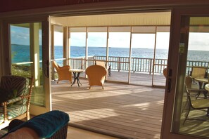 A covered outdoor deck with wooden flooring, wicker furniture, and a view of the ocean.