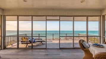 A covered outdoor area with a view of the ocean, featuring a wooden deck and two lounge chairs.