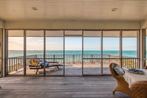 Un espacio al aire libre cubierto con vista al océano, que cuenta con una terraza de madera y dos sillones de descanso.