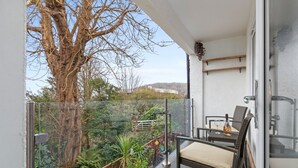 Uma varanda com guarda-corpo de vidro, uma cadeira de vime e uma mesa com uma garrafa e um copo.