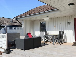 A covered outdoor patio with a table and chairs, a covered seating area, and a white building with a red door. - 4 Person Holiday Home in Laholm (Skummesloevsstrand)