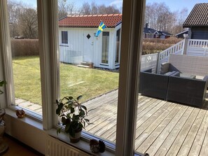 A view from a window overlooking a wooden deck, a small white building with a red roof, and a flag. - 4 Person Holiday Home in Laholm (Skummesloevsstrand)