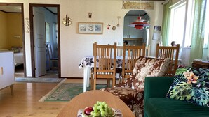 Una sala de estar con una mesa de madera, un sofá verde y un comedor con sillas de madera.