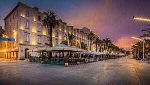A hotel with outdoor seating, palm trees, and a sunset sky. - Modern Comfort in Heart of Split (Split)