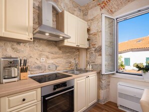 Eine Küche mit Steinwänden, einem eingebauten Ofen, einer Kaffeemaschine und einem Fenster mit Blick auf ein Haus.