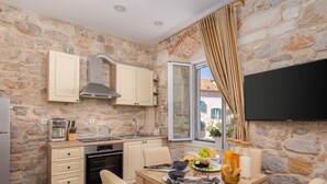 A stone-walled kitchen with a built-in oven, a dining table with chairs, and a TV mounted on the wall. - Modern Comfort in Heart of Split (Split)