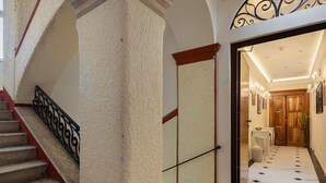 A staircase with a red handrail and black balusters, leading to a room with a wooden door and a chandelier. - Modern Comfort in Heart of Split (Split)