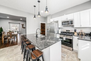 A modern kitchen with a central island, stainless steel appliances, and a dining area with wooden chairs. - Sleeps 10 Near OSU & Short North Spacious Modern Home Columbus (Columbus)