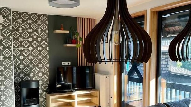 A modern living room with a wooden dining table, black leather sofa, and a television on a wooden stand. - Apartments pri fencu (Jesenice)