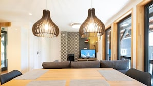 A dining area with a wooden table, two hanging pendant lights, and a television in the background. - Apartments pri fencu (Jesenice)