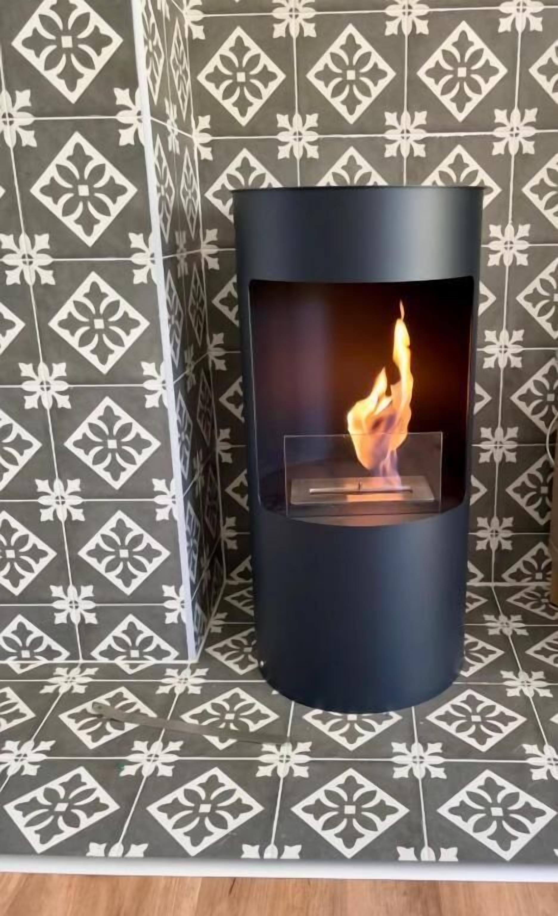 A modern fireplace with a clear glass front, set against a patterned wall.