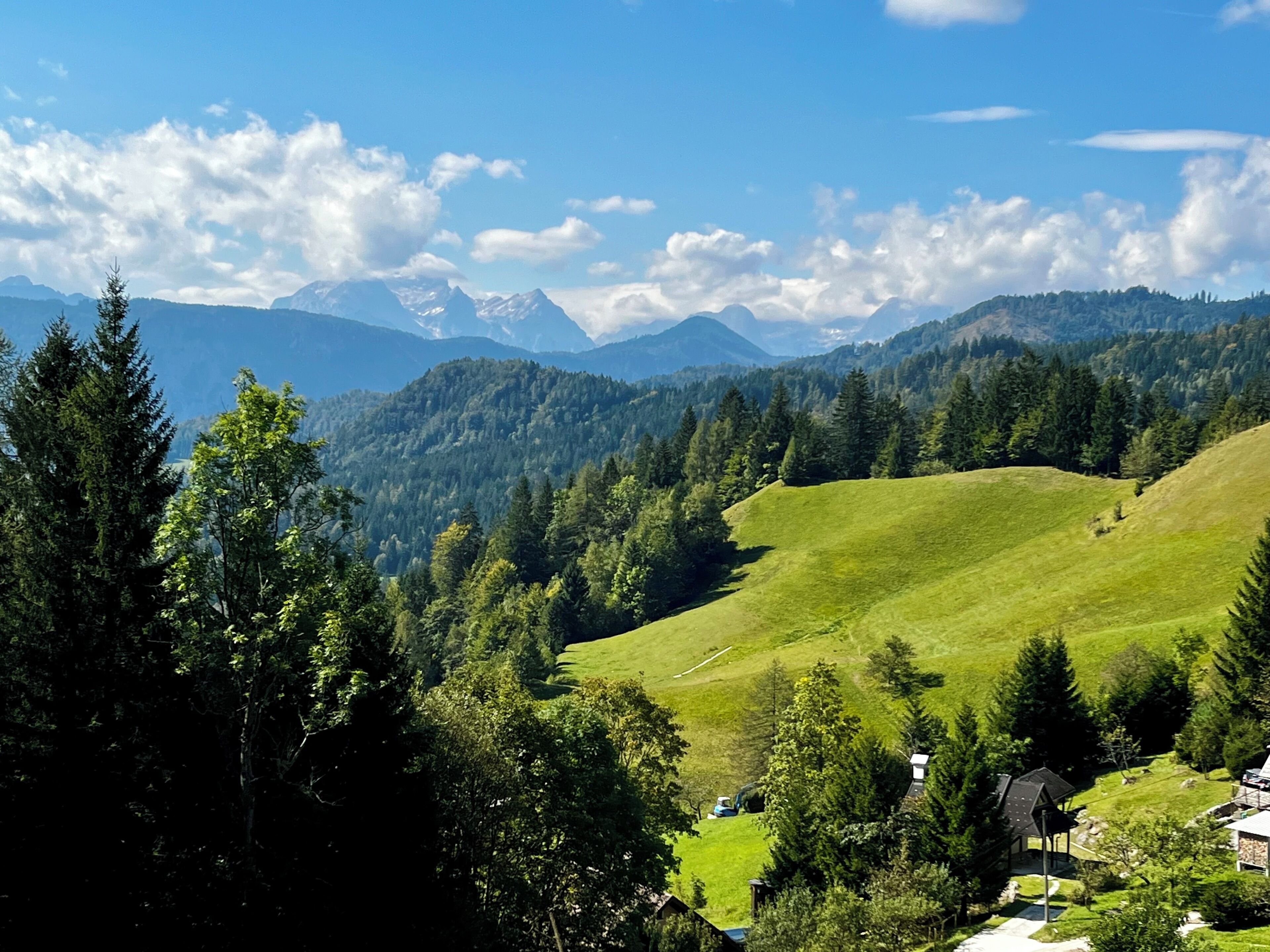 A mountainous landscape with a clear sky, green fields, and a small building with a roof.
