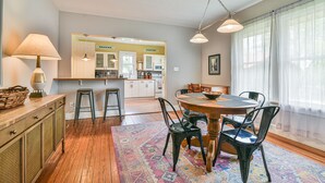 Een eetruimte met een houten tafel, stoelen, een vloerkleed en een keuken op de achtergrond.