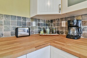 A kitchen with a stone backsplash, a toaster, a coffee maker, and jars on the counter. - Family-Friendly 3BR with Patio & Fenced Backyard (Asheville)
