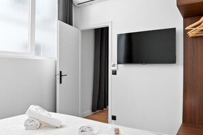 Een hotelkamer met een bed, een aan de muur bevestigde televisie, een deur naar een andere kamer en een raam.