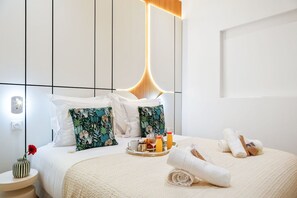 Et moderne hotelværelse med en pænt redt seng, et sengebord med en vase og et bakke med morgenmadsprodukter.