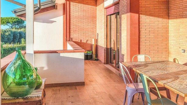 Un patio amplio con mesa y sillas de madera, un florero verde y vistas al exterior.