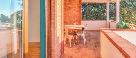 A modern interior with a wooden floor, a dining table with chairs, a brick wall, and a glass door leading outside.