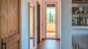 Un pasillo con una puerta de madera, una puerta de cristal que da a un balcón y una estantería llena de libros.