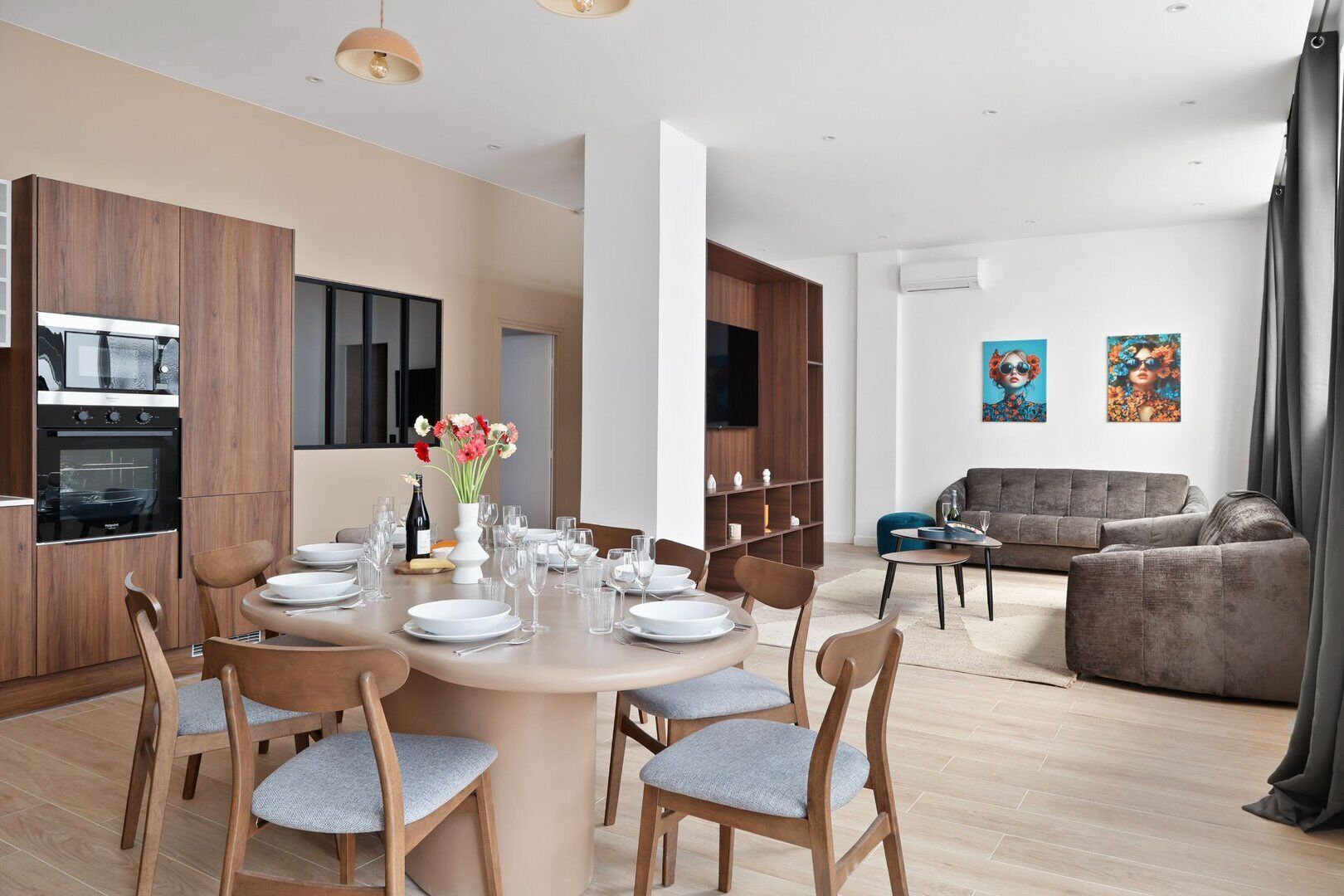 A modern kitchen with built-in appliances, a dining area with a round table and chairs, and a living room with a sofa and artwork.