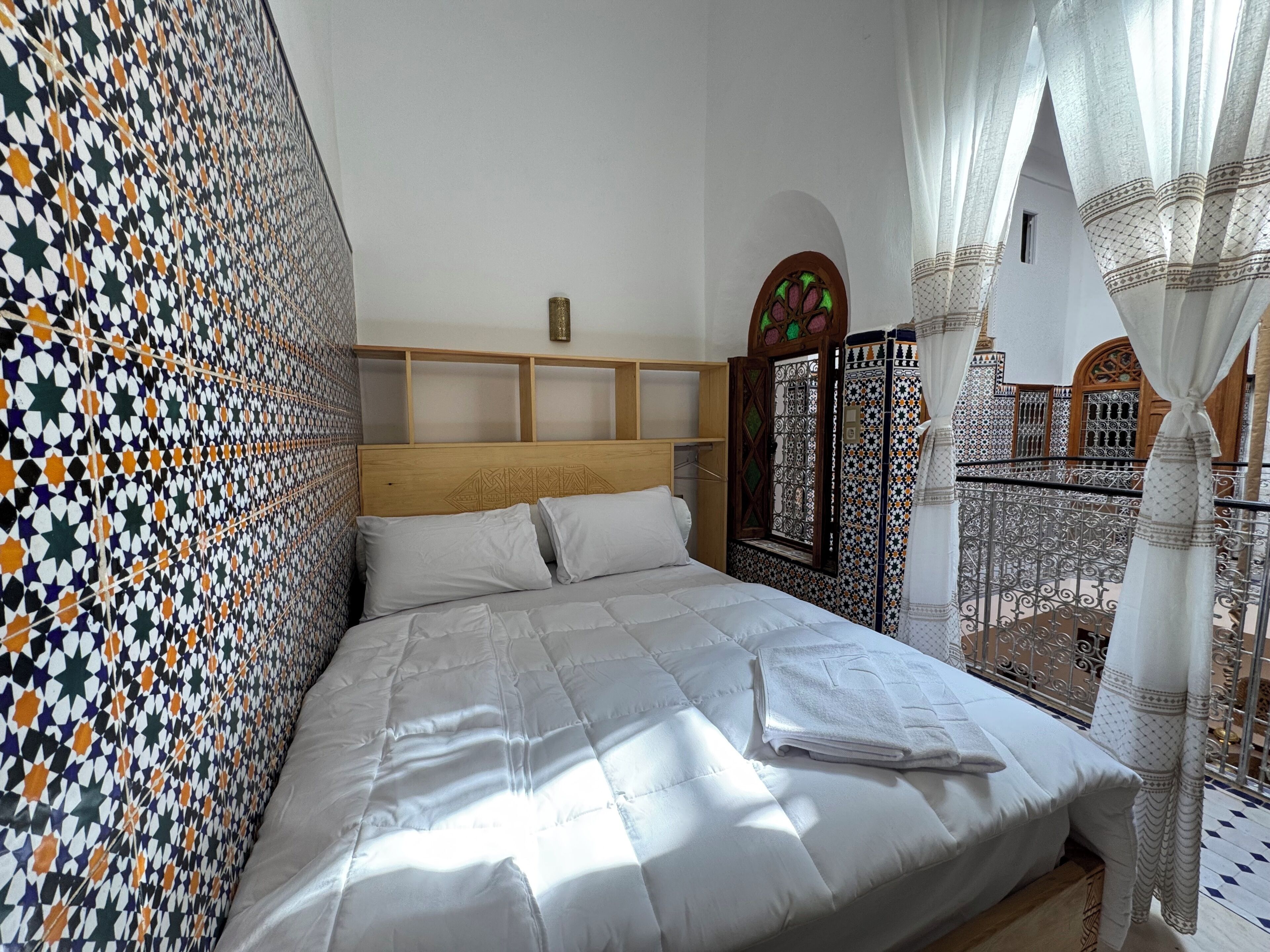 Un letto con biancheria bianca, una parete decorata e vista su un balcone con ringhiera.