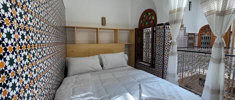 Un letto con biancheria bianca, una parete decorata e vista su un balcone con ringhiera.