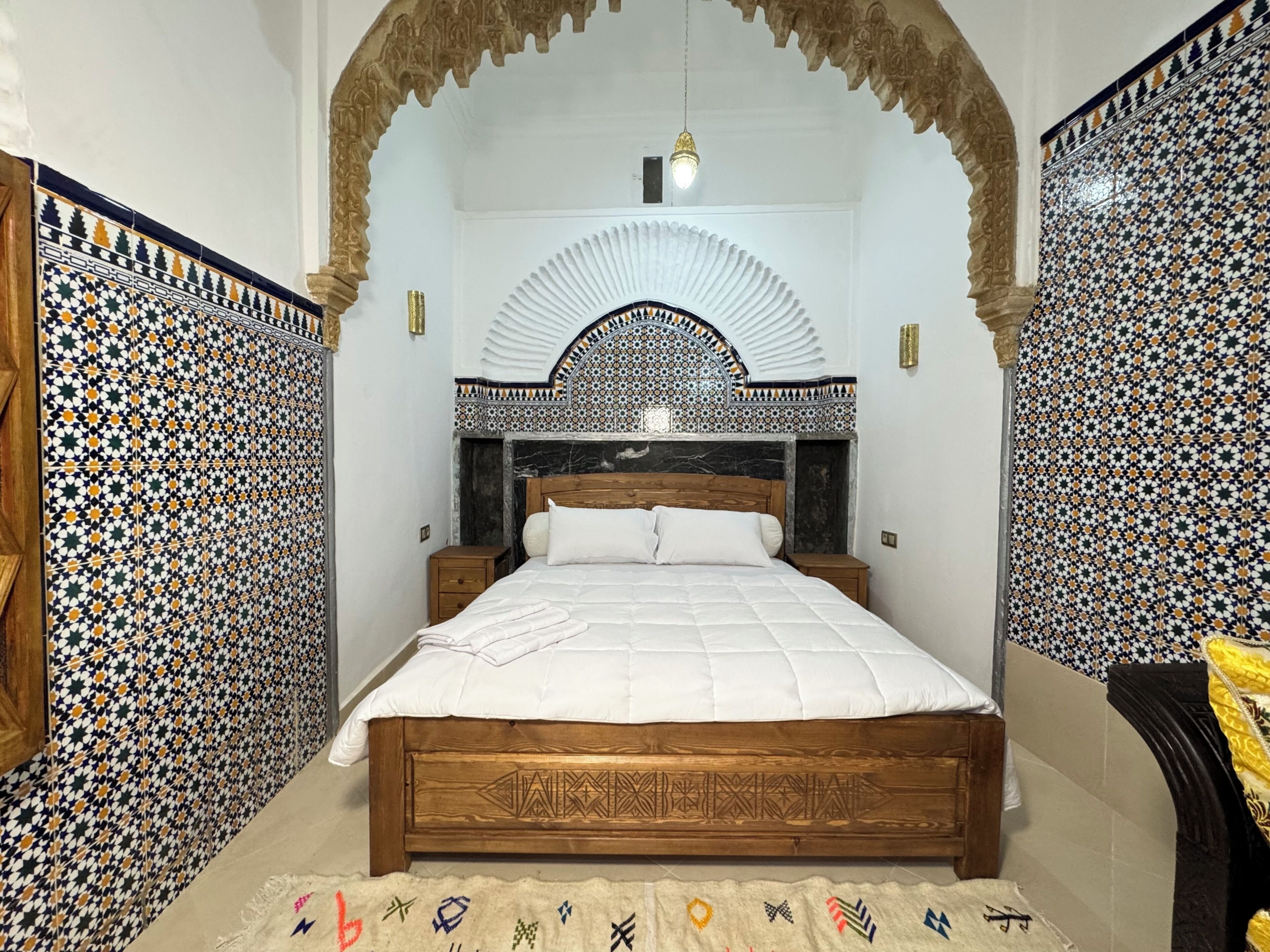 Ein Schlafzimmer mit einem hölzernen Bett, einem dekorativen Kopfteil und einem Wandmuster.