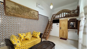 A room with a patterned wall, a sofa with yellow cushions, a wooden cabinet, and a staircase.