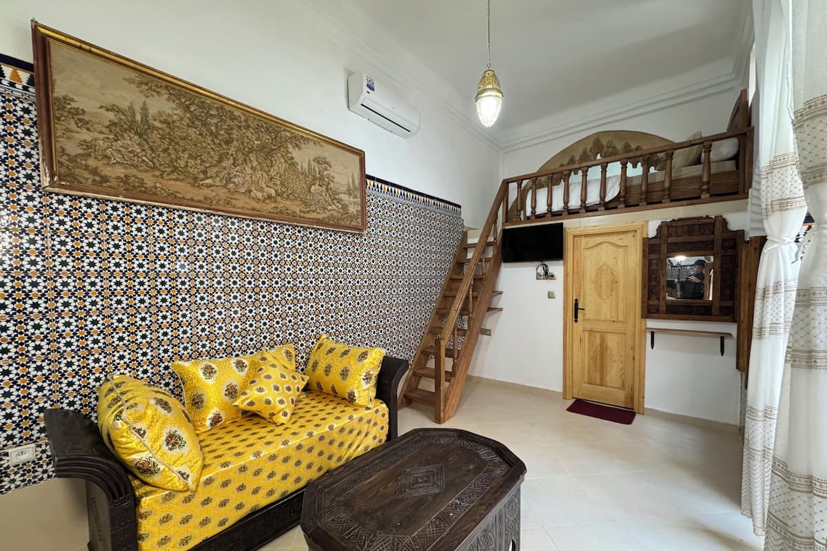 Una habitación con pared estampada, un sofá con cojines amarillos, un mueble de madera y una escalera.