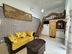 A room with a patterned wall, a sofa with yellow cushions, a wooden cabinet, and a staircase. - Riad AYA (Rabat)