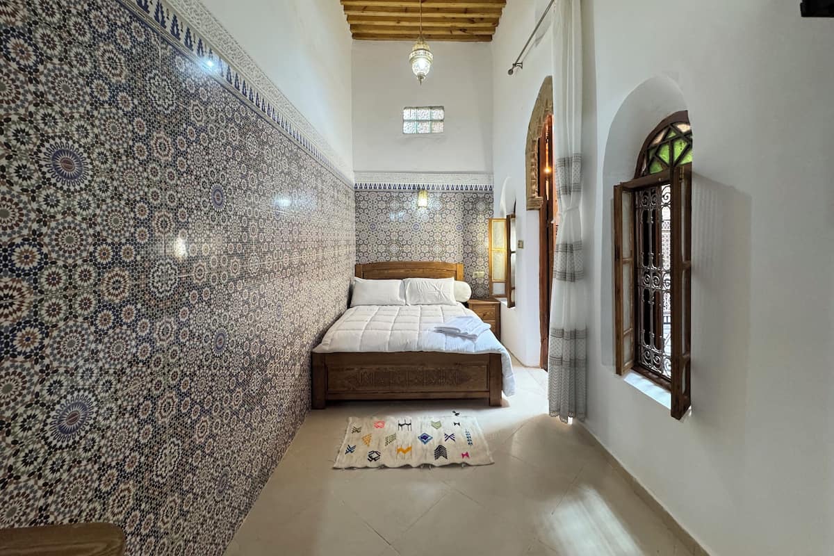 Un dormitorio con pared estampada, cama de madera, una alfombra pequeña y ventana con vistas.