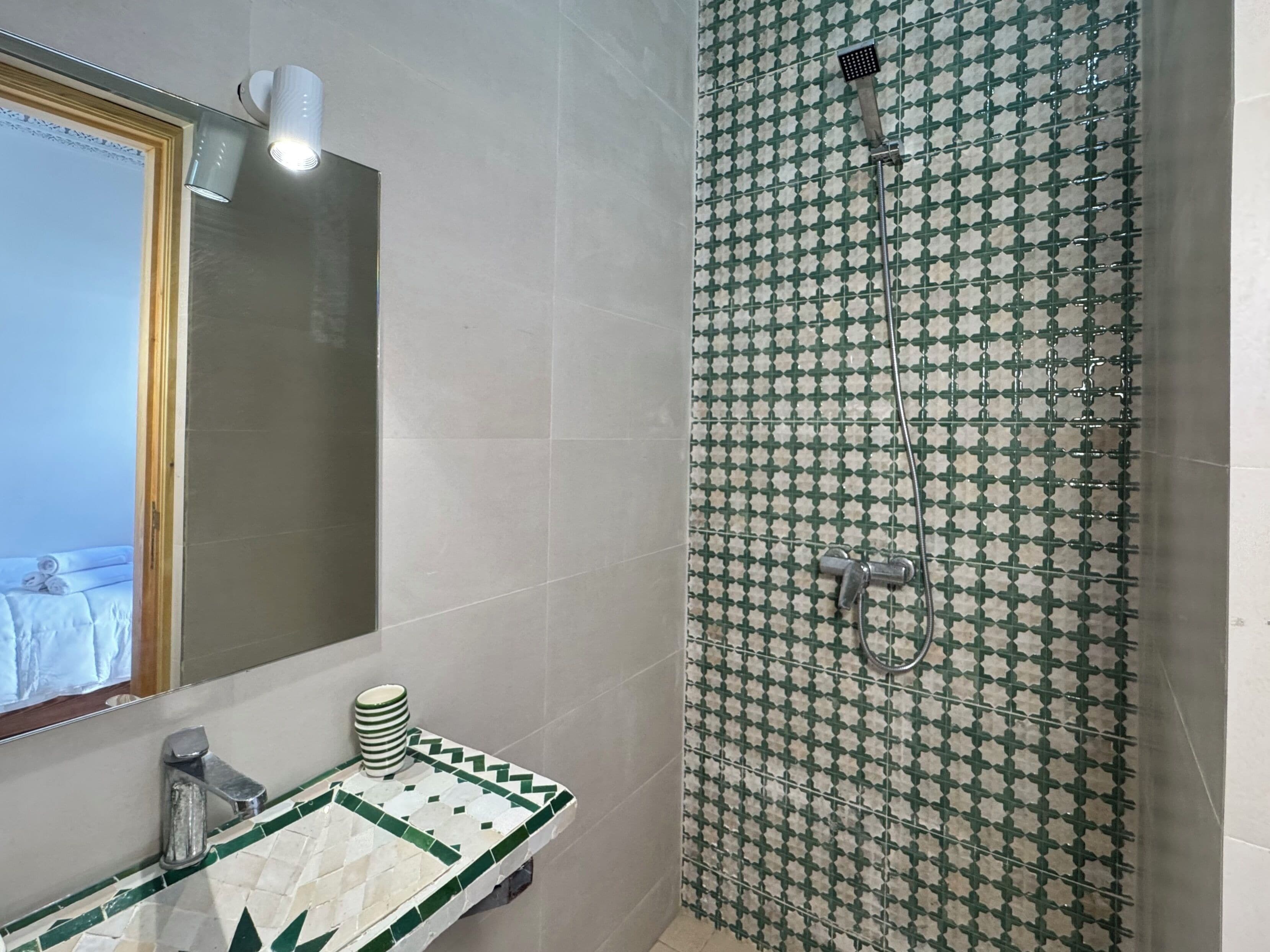 A bathroom with a shower, a sink with a mirror, and a tiled wall.
