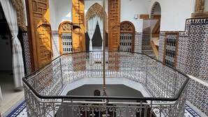 A multi-level interior with ornate metal railings, a central chandelier, and a patterned floor.