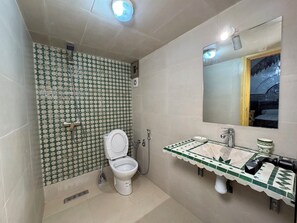 Un bagno con parete decorata, un water, una doccia, un lavandino con schienale in piastrelle decorative e uno specchio.