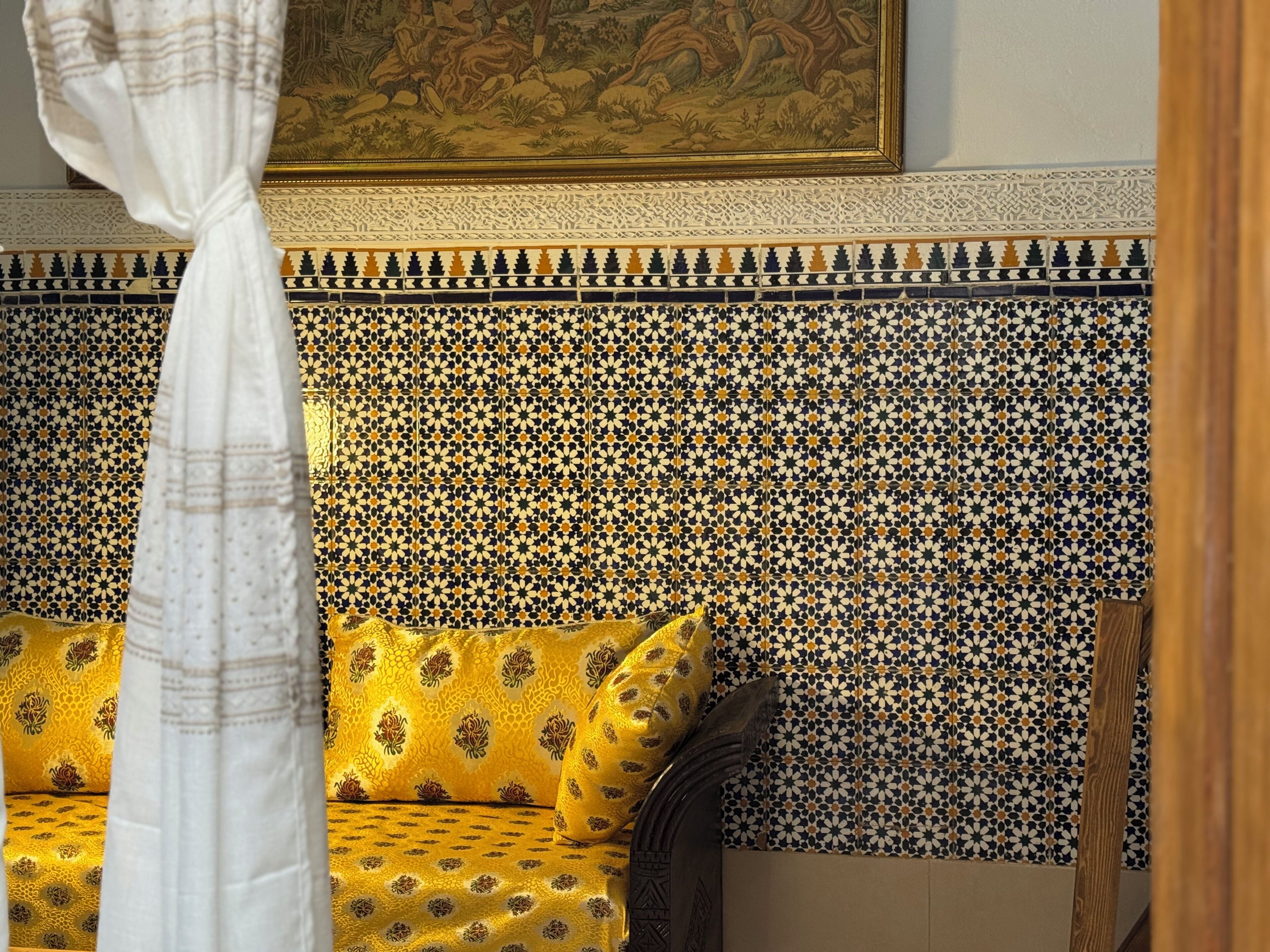 A room with a patterned headboard, a yellow sofa, and a curtain.