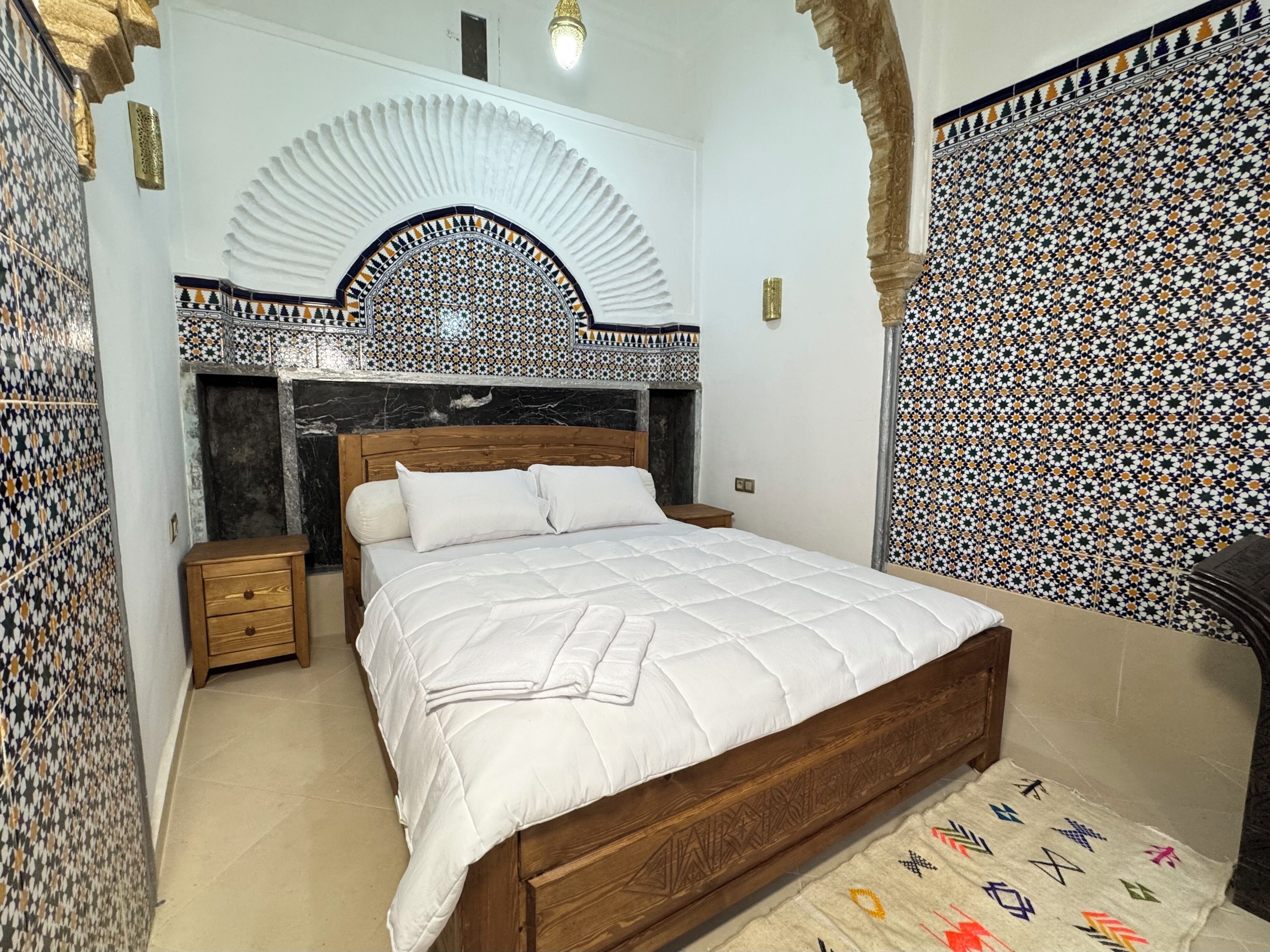 A bedroom with a bed, nightstands, a decorative arch, and patterned walls.