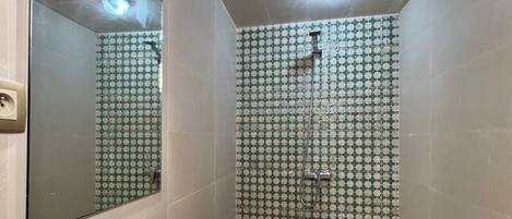 A bathroom with a shower, a sink with a mirror, and patterned tiles.