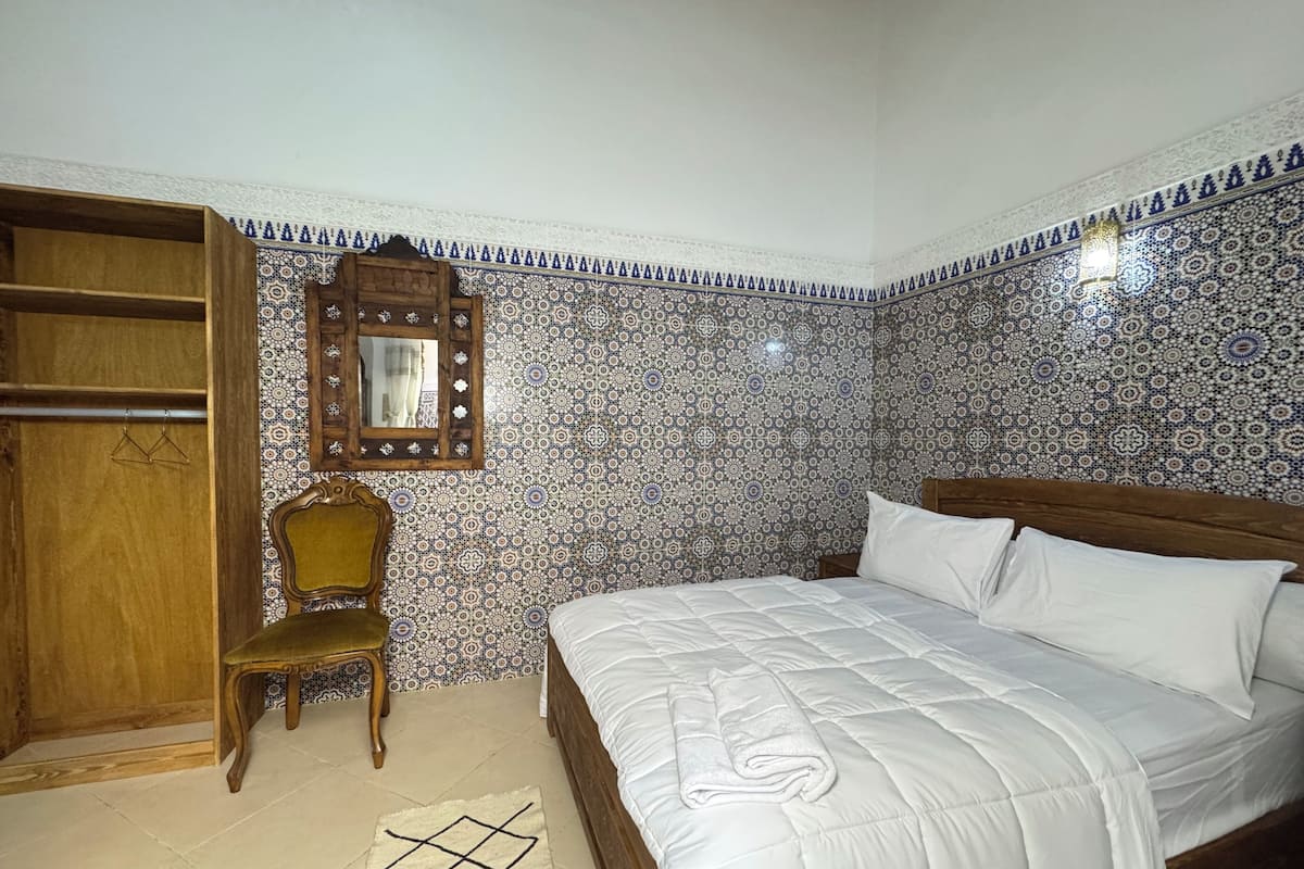 Un dormitorio con cama, armario de madera, una silla, espejo y paredes con diseño.