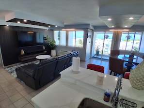 A modern living room with a black leather sofa, a flat-screen TV, a dining area with a white table and chairs, and large windows offering a view of the outdoors. - NEWLY RENOVATED, Tranquil oceanview gated community. Close to Beach and Airport (Río Grande)