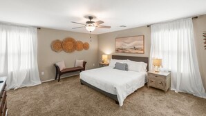 Ein Schlafzimmer mit Bett, Nachttischen, einer Bank, einem Deckenventilator und Wanddekoration.