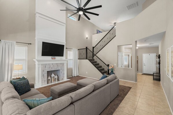 A spacious living room with a fireplace, a large sofa, a TV, and a staircase. - Desert Sky Escape in Marana (Marana)
