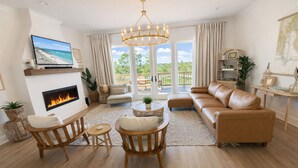 A living room with a fireplace, leather sofa, wooden chairs, and a large window with a view. - Lux home, walkable to priv beach, near marina, golf in Gulf Shores Fort Morgan (Gulf Shores)