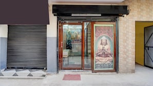 A building entrance with a closed shutter, a glass door, and a Buddha statue. - Hotel O Isbt Sector 43 Bus Terminal (Chandigarh)