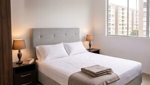 Quarto de hotel moderno com uma cama grande, duas mesas de cabeceira, uma janela com vista para a cidade e uma luminária no teto.