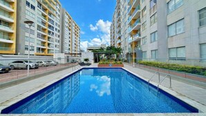 Um edifício de apartamentos moderno com piscina central, varandas e céu claro.