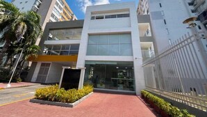Um edifício moderno com entrada de vidro, rodeado por um caminho de tijolos e uma cerca de metal.