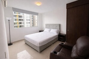 Una camera da letto con un letto, comodini, un armadio, una sedia, una lampada da terra e una finestra con vista sugli edifici.