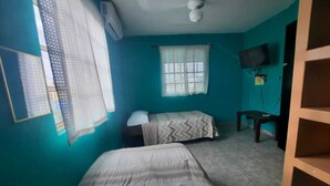 Una habitación con dos camas, un escritorio, un televisor y una ventana con cortinas.