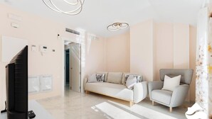 Un salon moderne comprenant un canapé, un fauteuil, un téléviseur et une porte donnant sur une autre pièce.