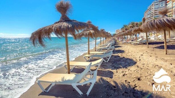 Une plage avec des chaises longues blanches et des parasols en chaume.